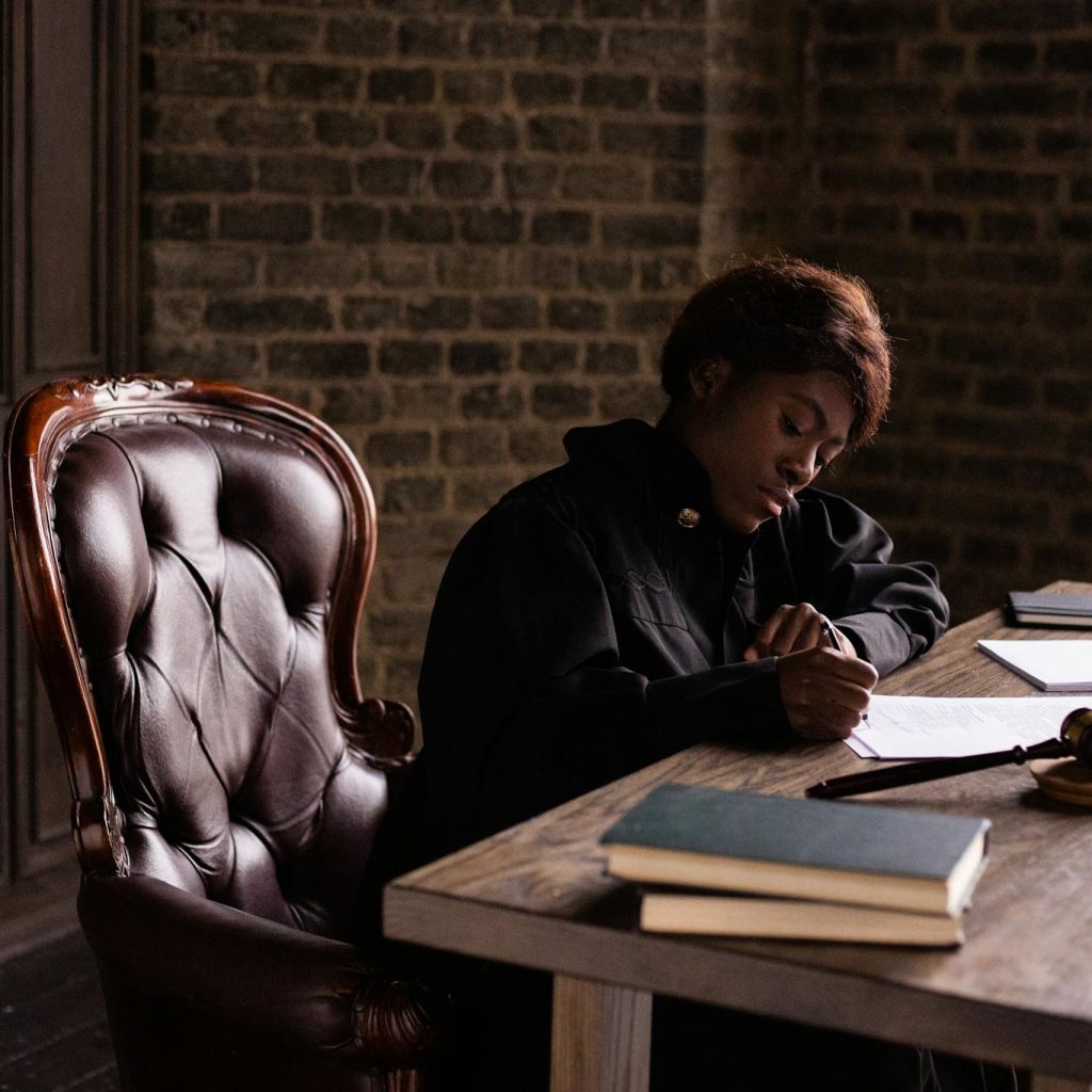 Black female judge in judicial robe writing at desk in an office setting, focusing on legal work.