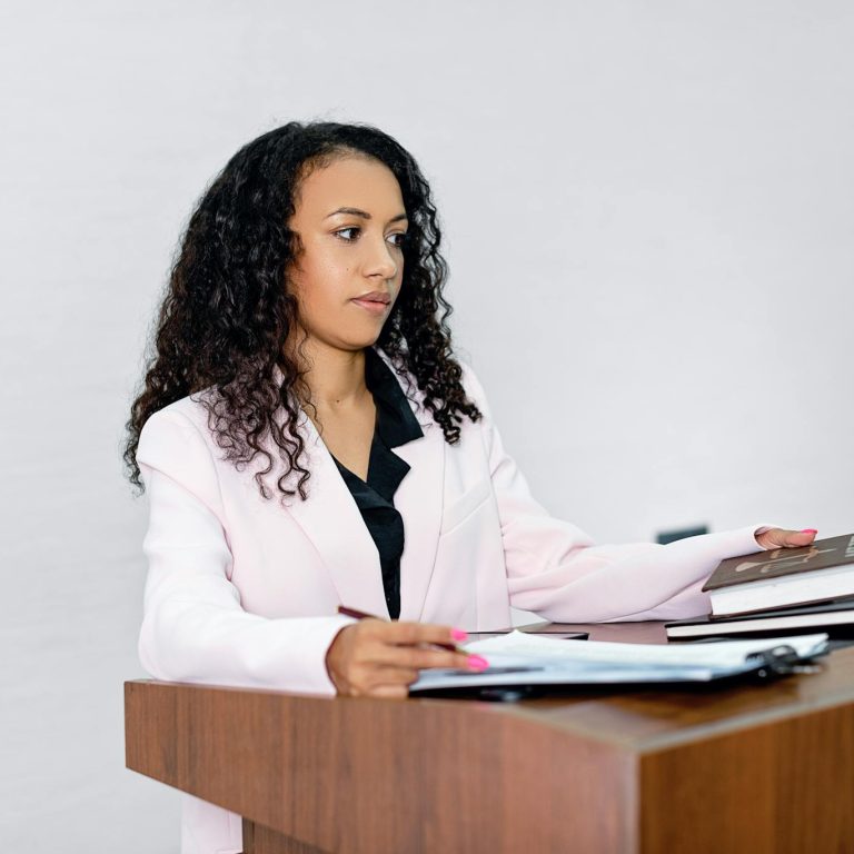 A professional black woman lawyer presenting documents at a podium with books.