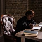 Black female judge in judicial robe writing at desk in an office setting, focusing on legal work.
