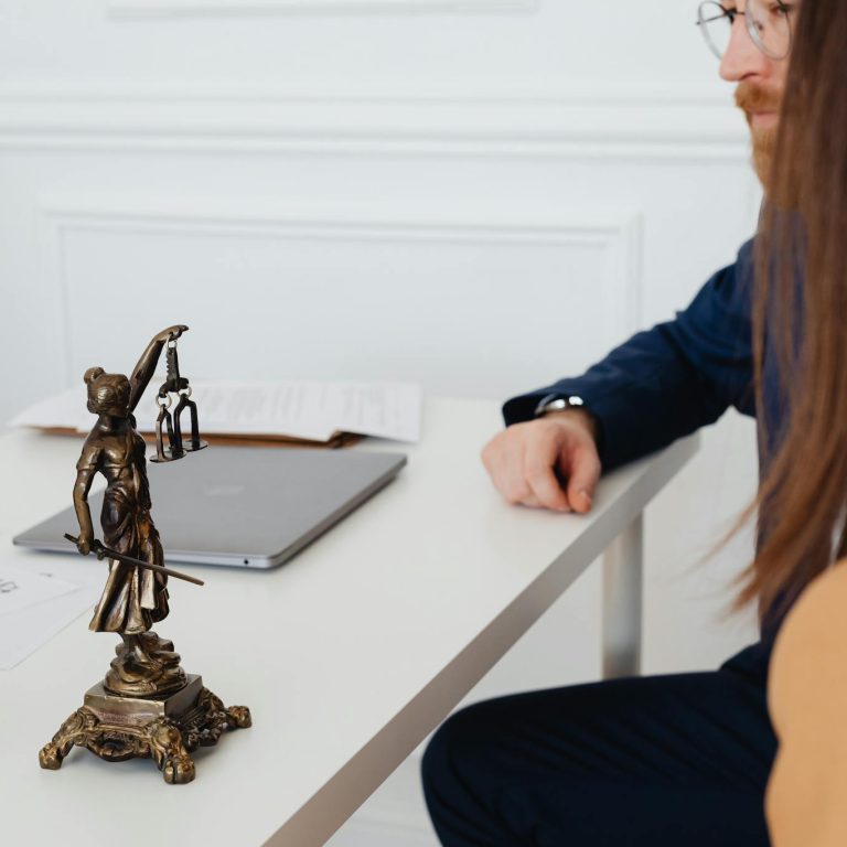 Professional setting with lawyers and Lady Justice statue discussing legal documents.