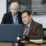 Smart mature ethnic judge in suit working on laptop and discussing details of new case with young female assistant in law firm